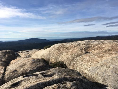 A panoramic view of rocky terrain with distant hills and a blue sky, showcasing nature's rugged beauty.