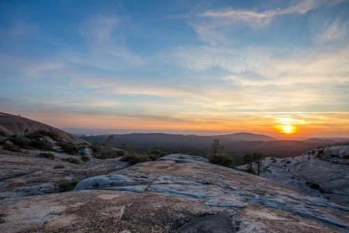 A scenic view of a rocky landscape at sunset, with vibrant colors in the sky and distant mountains.