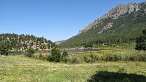 A serene landscape featuring a lake surrounded by mountains and lush greenery under a clear blue sky.