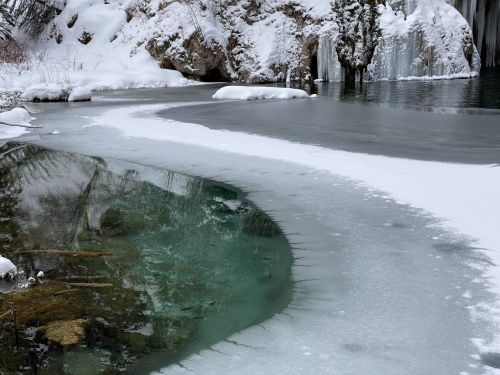 A serene winter scene featuring a partially frozen lake with snow-covered banks and icy cliffs in the background.