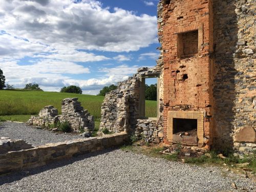 Ruins of a stone building with a partially collapsed wall, set against a grassy field and blue sky.