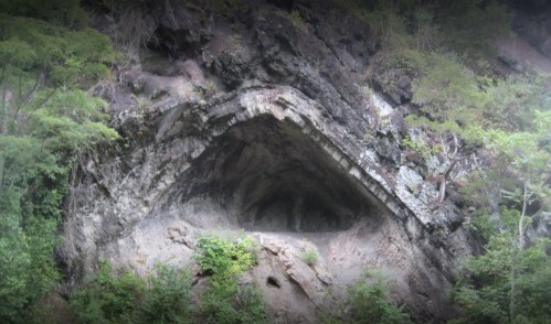 A rocky cliff with a large, eye-shaped cave entrance surrounded by greenery.