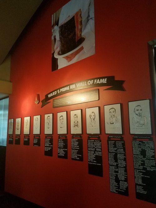 A red wall featuring "Ward's Prime Rib Wall of Fame" with framed portraits and names of honorees.