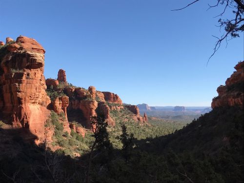 A scenic view of red rock formations and green trees under a clear blue sky in a canyon landscape.