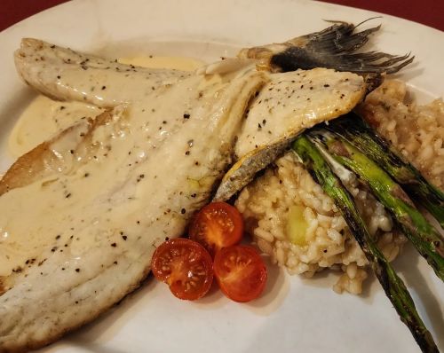 A plate featuring grilled fish with creamy sauce, asparagus, risotto, and cherry tomatoes.