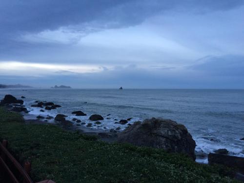 A serene coastal scene at dusk, featuring rocky shores and calm waters under a cloudy sky.
