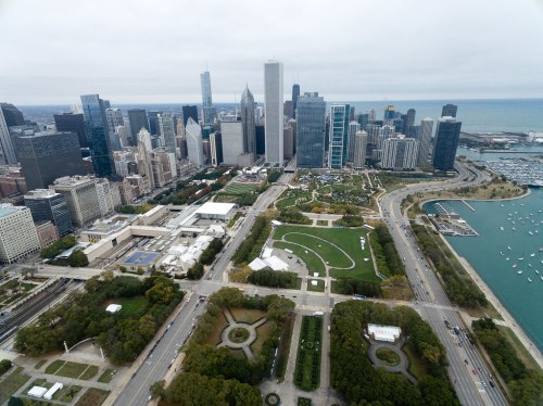 Aerial view of Chicago's skyline, featuring parks, roads, and Lake Michigan in the background under a cloudy sky.
