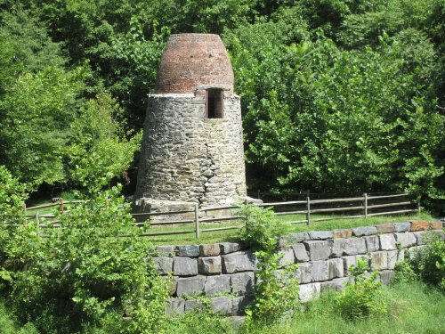 A stone and brick structure surrounded by greenery, with a fenced area and a stone wall in the foreground.