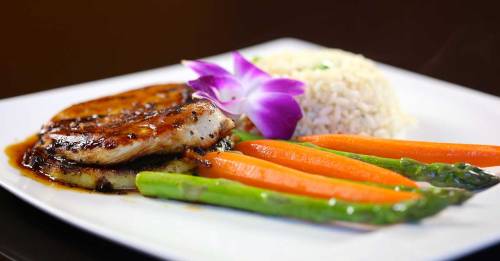 Grilled chicken with a sweet glaze, served with rice, carrots, asparagus, and a purple flower garnish.