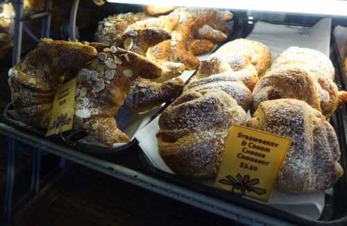 A display of freshly baked croissants, including a strawberry and cream cheese variety, with price tags.