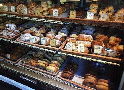 A display case filled with various baked goods, including pastries, bagels, and rolls, all neatly arranged on trays.