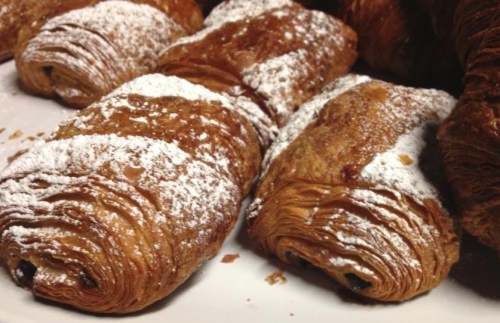 Close-up of flaky pastries dusted with powdered sugar, showcasing layers and a rich, golden-brown color.