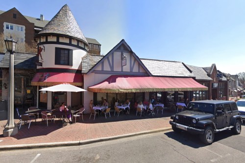 A quaint restaurant with a turret, outdoor seating, and a black Jeep parked nearby on a sunny day.