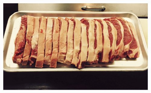 A tray of neatly arranged raw beef steaks with visible marbling and fat.