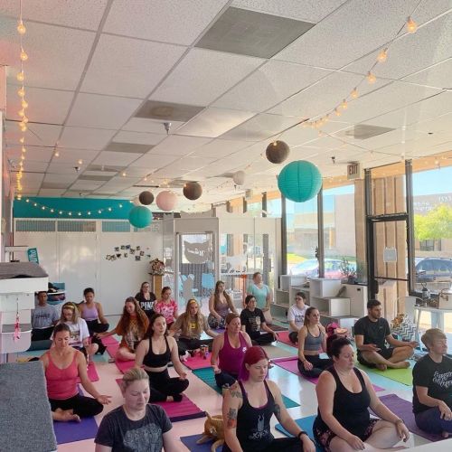 A group of people practicing yoga and meditation in a bright, colorful studio with string lights and decorative lanterns.