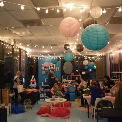 A cozy indoor space decorated with colorful lanterns and string lights, filled with people socializing and relaxing.