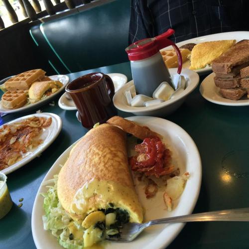 A table with plates of breakfast food, including an omelet, waffles, toast, and coffee.
