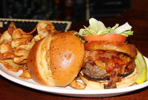A juicy burger with lettuce, tomato, onion rings, and bacon, served with a side of crispy potato chips on a plate.