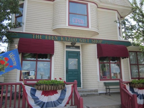 Exterior of The Eden Kazoo Gift Shop, featuring an "Open" sign, red awnings, and decorative bunting.