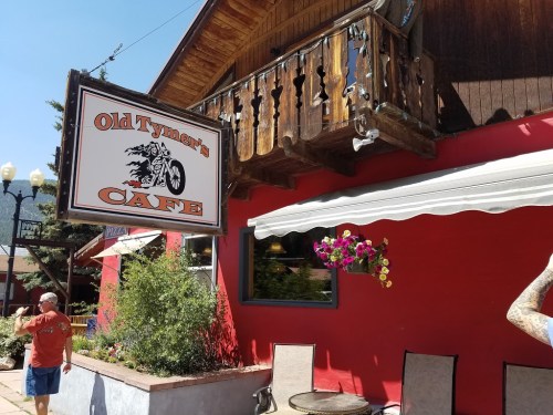 Sign for "Old Tymer's Cafe" on a red building, with a balcony and hanging flower basket. A person walks by.
