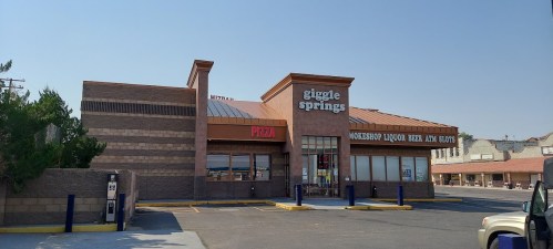 Exterior of a building featuring "Giggle Springs" and a liquor store, with a parking lot in front.