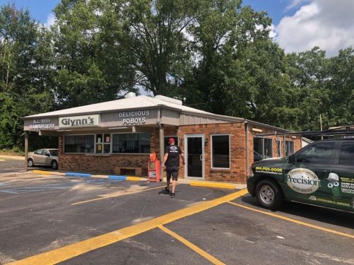 A man walks towards Glynn's, a casual eatery with a sign for hamburgers and poboys, surrounded by trees.