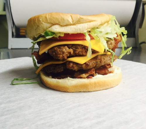 A stacked burger with two beef patties, cheddar cheese, lettuce, and tomato, served on a soft bun.