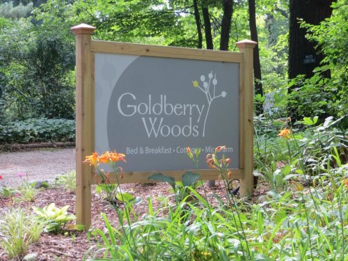 Sign for Goldberry Woods Bed & Breakfast, surrounded by greenery and flowers.