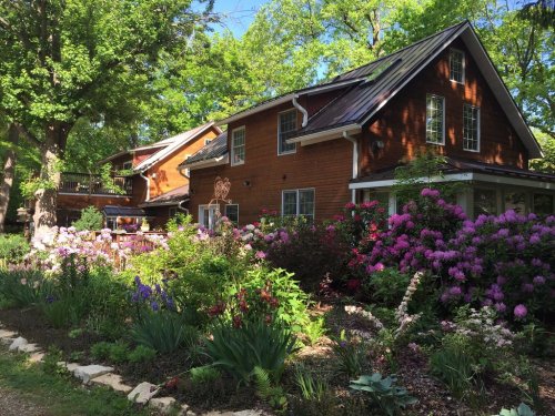 A charming wooden house surrounded by vibrant flowers and lush greenery on a sunny day.
