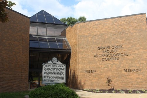 Exterior view of the Grave Creek Mound Archaeological Complex, featuring a modern building with a glass roof and brick walls.