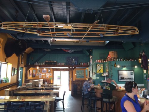 Interior of a rustic bar with wooden decor, a canoe hanging from the ceiling, and patrons seated at the counter.