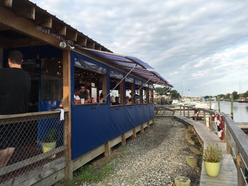 A waterfront restaurant with outdoor seating, surrounded by boats and a cloudy sky.