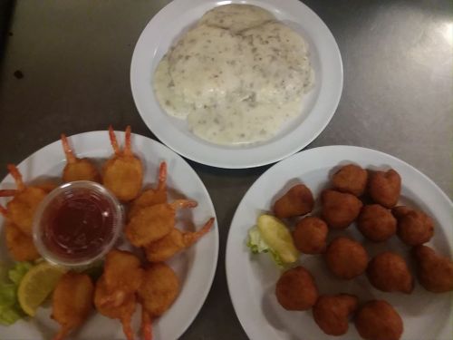 Two plates of food: one with fried shrimp and cocktail sauce, the other with fried balls and a side of creamy gravy.