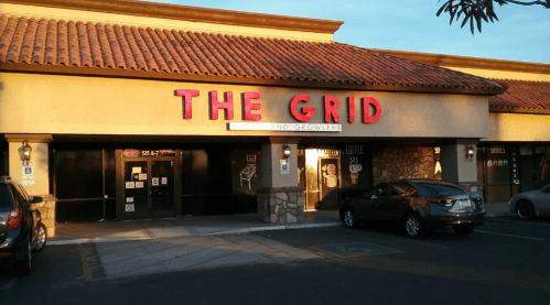 Exterior of a building with a sign reading "THE GRID" and a parking lot, featuring a warm sunset glow.