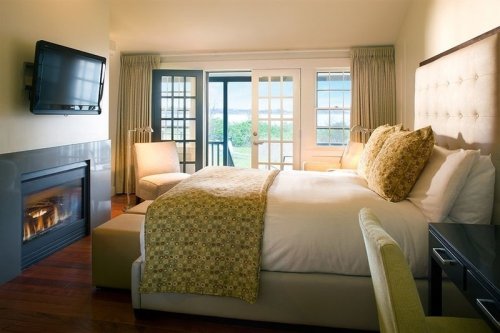 Cozy bedroom with a large bed, fireplace, TV, and balcony doors overlooking a scenic view.
