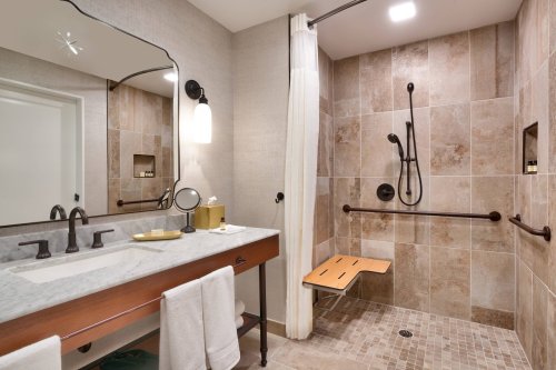 Modern bathroom featuring a walk-in shower, marble sink, and accessible design elements.