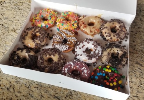 A box of assorted donuts with various toppings, including sprinkles, chocolate chips, and icing, on a granite surface.