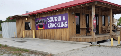 A wooden building with a red roof, featuring a sign that reads "Hebert's Boudin & Cracklins."