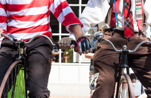 Two cyclists hold hands while riding, one in a red and white striped shirt and the other in a white shirt with a tie.