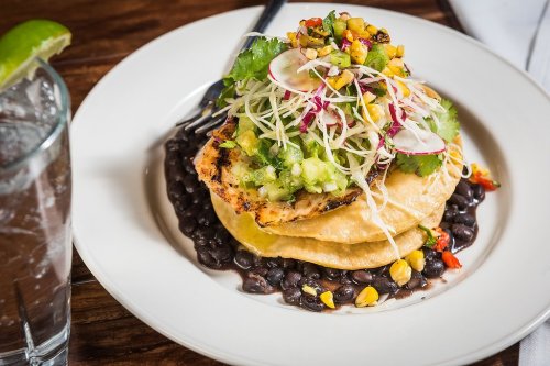 A plate of grilled fish on a crispy tortilla, topped with fresh salsa, greens, and served with black beans.