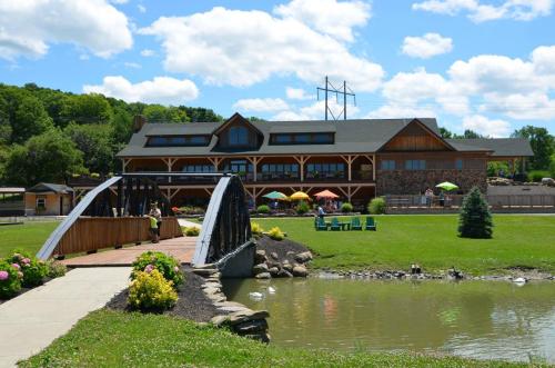 A scenic view of a lodge with a bridge over a pond, surrounded by greenery and colorful umbrellas on a sunny day.