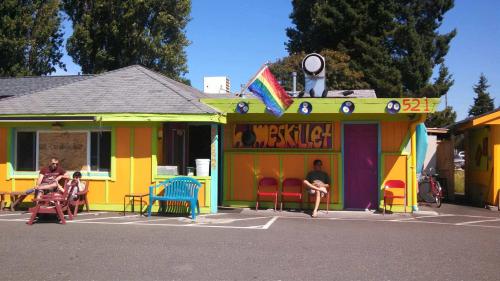 Colorful buildings with a rainbow flag, outdoor seating, and people relaxing in a vibrant, sunny setting.