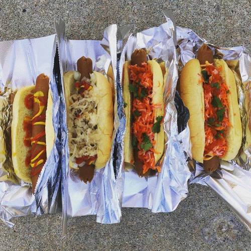 Four hot dogs in buns, each topped with different condiments: mustard, sauerkraut, and a colorful slaw.
