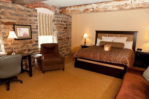 Cozy hotel room with a king bed, stone walls, a desk, and warm lighting.