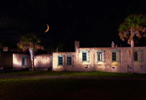 A moonlit scene of an old building with palm trees, illuminated against a dark night sky.