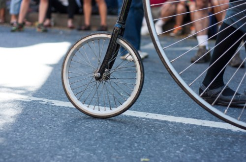 A close-up of a bicycle wheel on a street, with a blurred crowd in the background.
