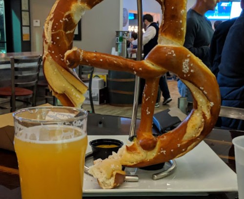 A large pretzel on a stand next to a glass of beer, set in a casual dining environment.