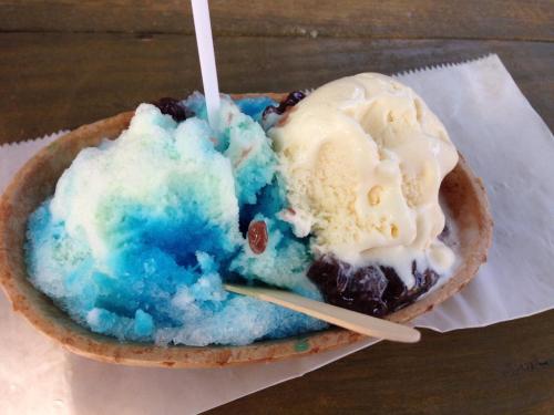A bowl of colorful shaved ice with blue and green layers, topped with vanilla ice cream and a spoon.