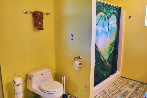 A bright yellow bathroom featuring a toilet, towel rack, and a shower curtain with a heart-shaped tree design.