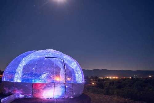 A glowing dome structure under a starry night sky, with distant mountains and city lights in the background.